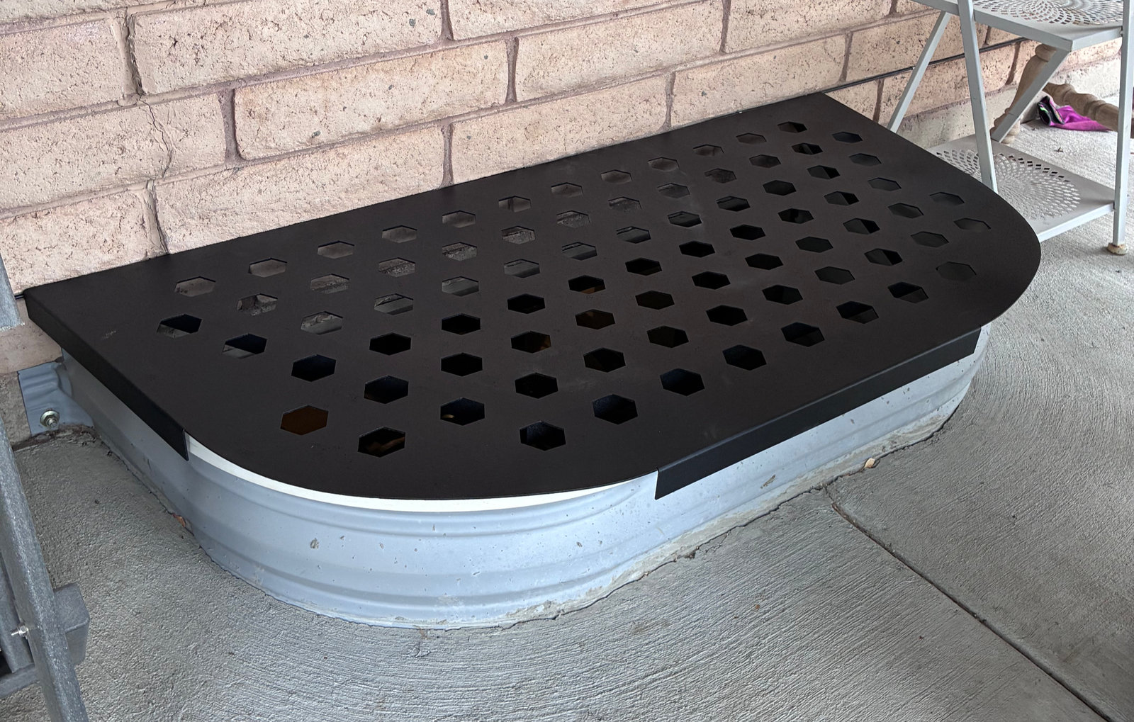 A custom laser-cut window well cover fitted over a galvanized well